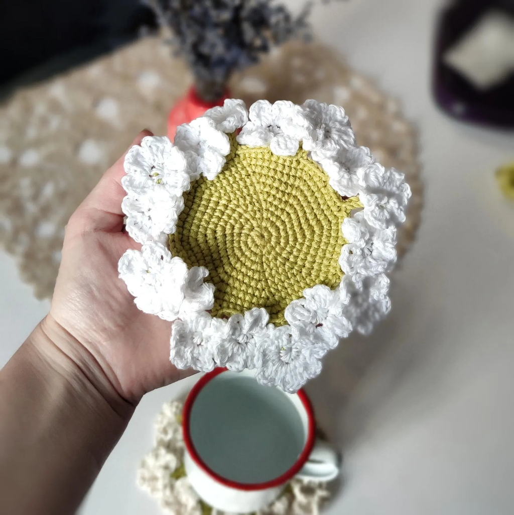 Flower crochet coaster with ruffled edge under coffee mug