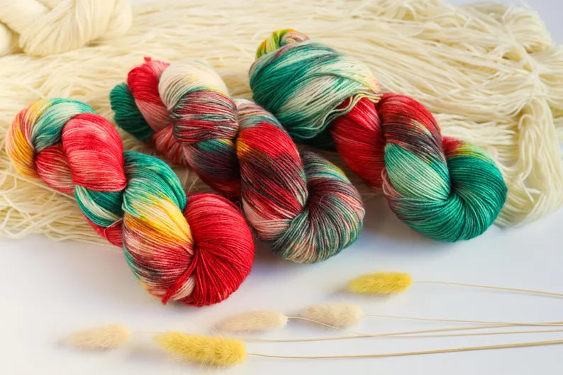 Christmas hand-dyed sock yarn in red, emerald green, golden yellow and ivory, variegated fingering weight superwash wool yarn for festive knitting.