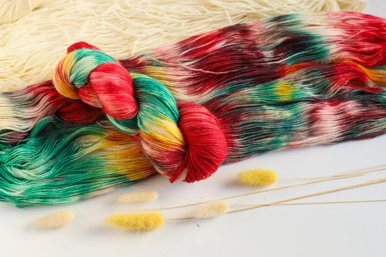 Christmas hand-dyed sock yarn in red, emerald green, golden yellow and ivory, variegated fingering weight superwash wool yarn for festive knitting.