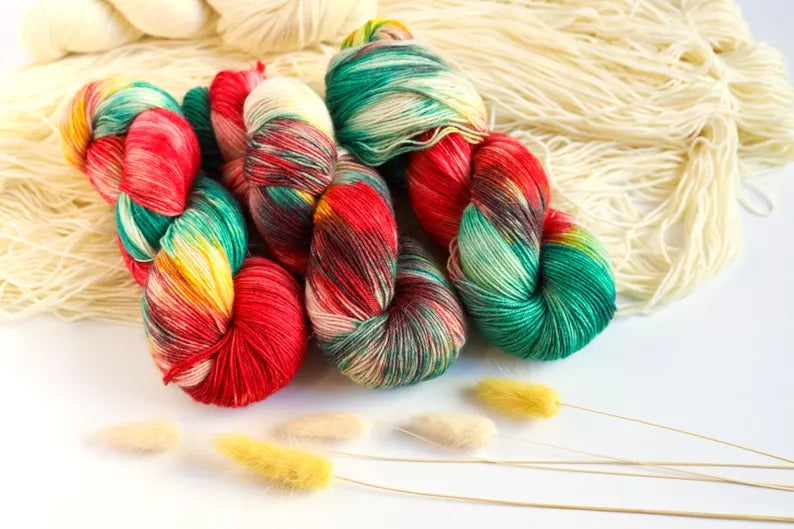 Christmas hand-dyed sock yarn in red, emerald green, golden yellow and ivory, variegated fingering weight superwash wool yarn for festive knitting.
