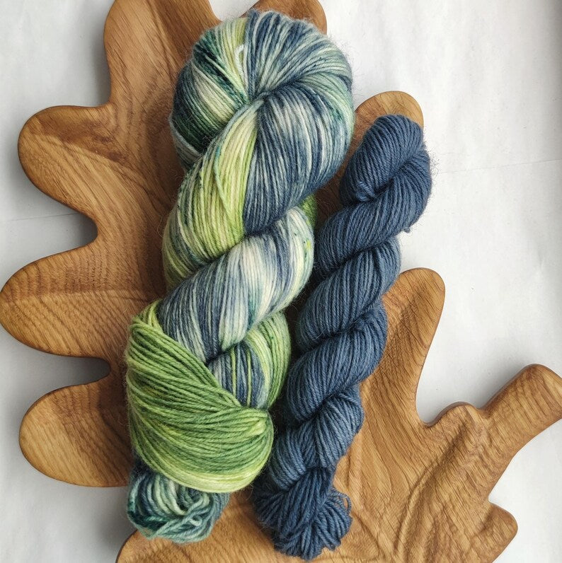 Full skein and mini skein sock yarn set with hand dyed variegated yarn in sage green, cream and blue-grey shades paired with a smoky blue mini skein.