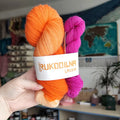 Bright orange hand-dyed sock yarn paired with a vibrant fuchsia mini skein, displayed as a fingering weight wool nylon yarn set for knitting and crochet projects.