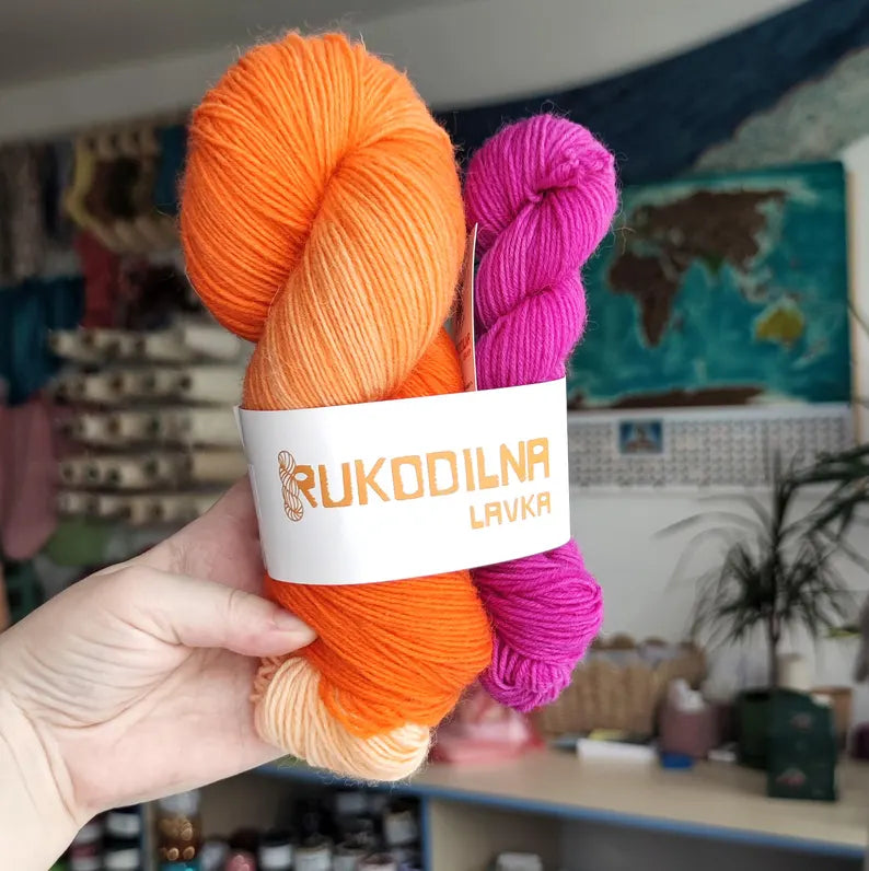 Bright orange hand-dyed sock yarn paired with a vibrant fuchsia mini skein, displayed as a fingering weight wool nylon yarn set for knitting and crochet projects.