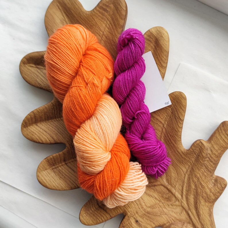 Bright orange hand-dyed sock yarn paired with a vibrant fuchsia mini skein, displayed as a fingering weight wool nylon yarn set for knitting and crochet projects.