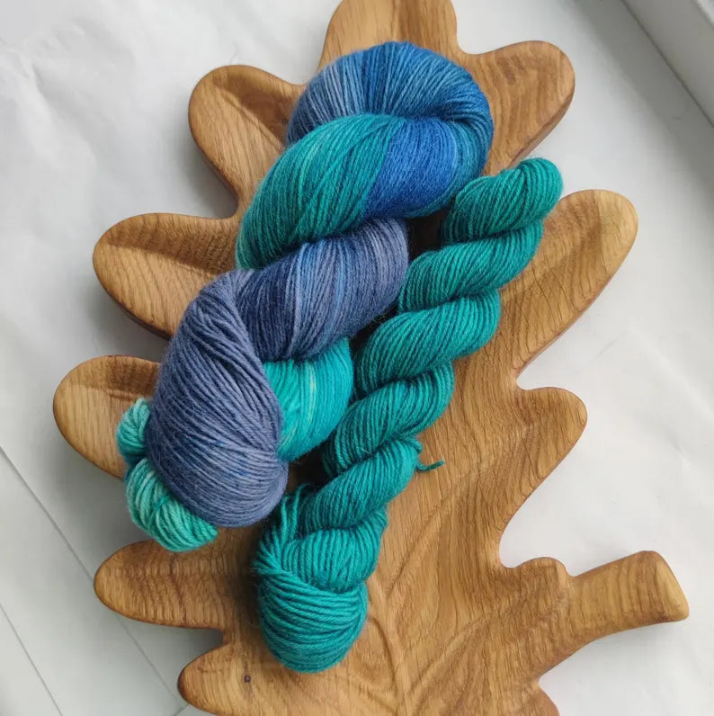 Hand dyed sock yarn set featuring a blue and turquoise variegated skein with a matching teal mini skein on a wooden leaf-shaped tray.