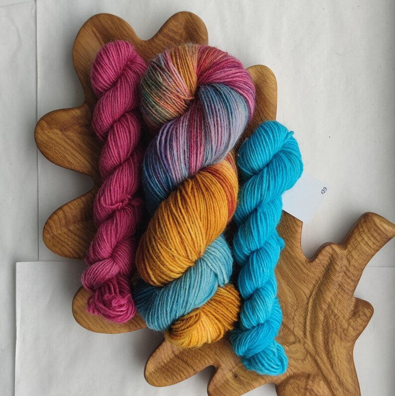 Hand dyed sock yarn set featuring a colorful variegated skein with pink, gold, turquoise and lavender shades paired with bright turquoise and berry pink mini skeins.