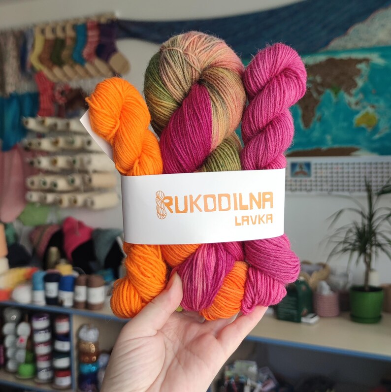 Hand dyed sock yarn gift set featuring a variegated skein in berry pink, orange and olive green shades paired with matching mini skeins. Fingering weight yarn bundle for knitters.