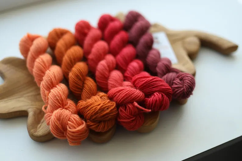 Hand dyed mini skein set featuring peach, terracotta, coral, raspberry and dusty rose sock yarn mini skeins arranged on a wooden leaf tray.