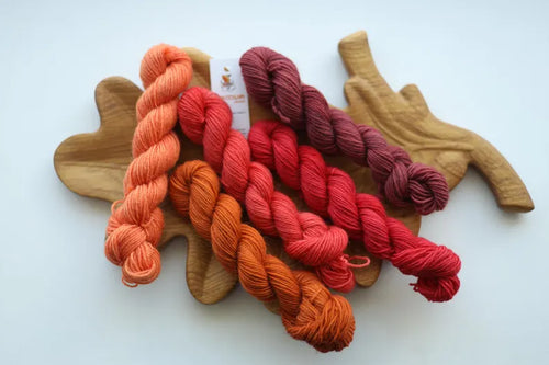 Hand dyed mini skein set featuring peach, terracotta, coral, raspberry and dusty rose sock yarn mini skeins arranged on a wooden leaf tray.