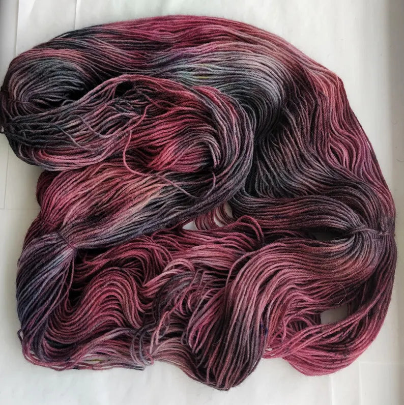 Hand-dyed sock yarn in blackberry, dusty rose and charcoal shades displayed as a variegated fingering weight wool nylon skein.