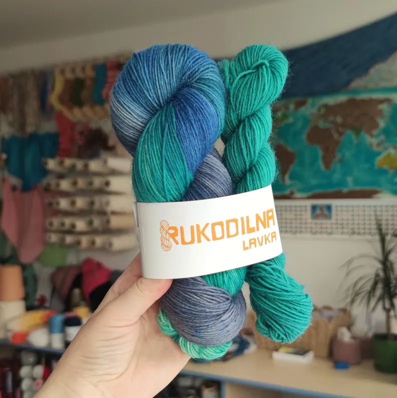 Hand dyed sock yarn set featuring a blue and turquoise variegated skein with a matching teal mini skein on a wooden leaf-shaped tray.