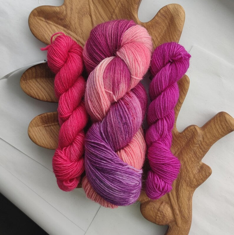 Hand dyed pink sock yarn set with one variegated skein and two matching mini skeins in shades of raspberry, blush pink, and orchid.