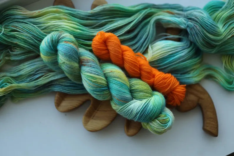 Hand dyed sock yarn set with one mint variegated 100g skein and one bright orange 20g mini skein on a wooden tray.