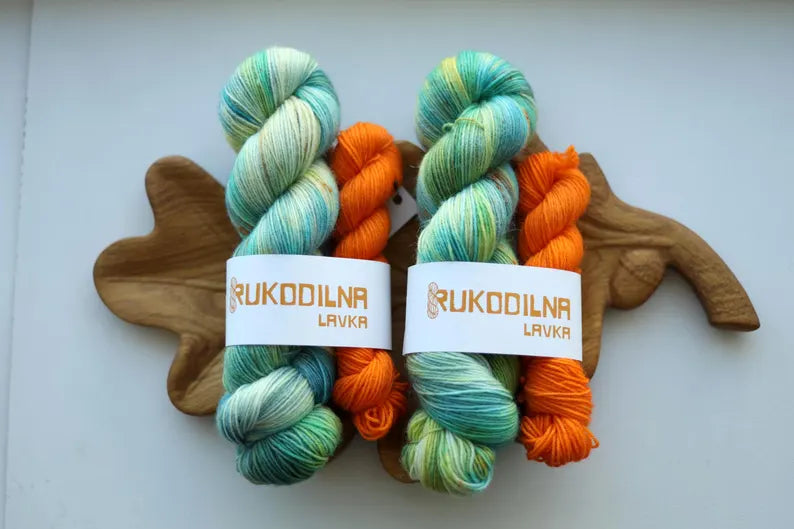 Hand dyed sock yarn set with one mint variegated 100g skein and one bright orange 20g mini skein on a wooden tray.