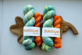 Hand dyed sock yarn set with one mint variegated 100g skein and one bright orange 20g mini skein on a wooden tray.