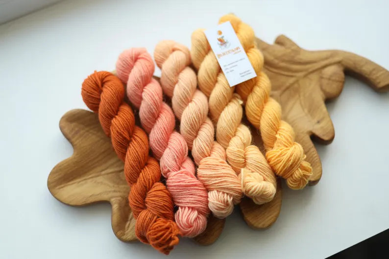 Hand dyed mini skein set featuring terracotta, coral, blush pink, peach and buttery yellow sock yarn mini skeins displayed on a wooden leaf tray.