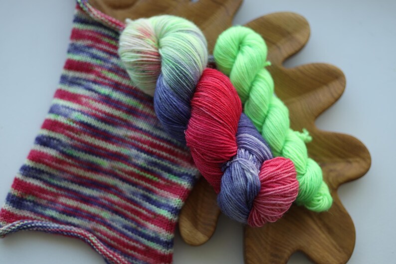 Hand dyed sock yarn set featuring vibrant purple, pink and lime green shades paired with a coordinating contrast mini skein. Perfect for colorful socks, shawls and accessories.