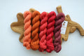 Hand dyed mini skein set featuring peach, terracotta, coral, raspberry and dusty rose sock yarn mini skeins arranged on a wooden leaf tray.