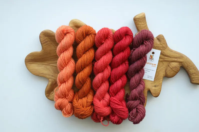 Hand dyed mini skein set featuring peach, terracotta, coral, raspberry and dusty rose sock yarn mini skeins arranged on a wooden leaf tray.
