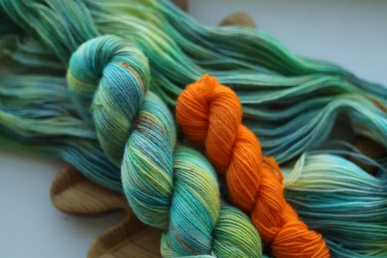 Hand dyed sock yarn set with one mint variegated 100g skein and one bright orange 20g mini skein on a wooden tray.
