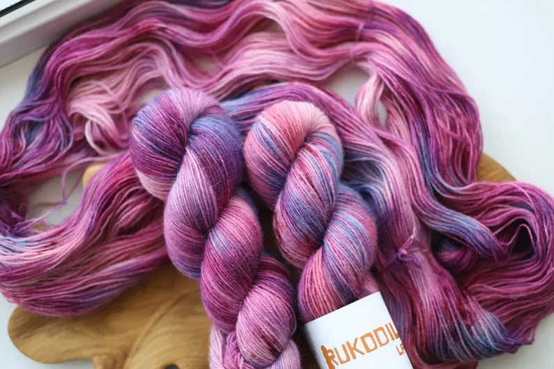 Hand dyed lilac sock yarn in soft purple, blush pink and lavender with delicate blue speckles, fingering weight wool nylon knitting yarn.