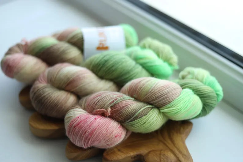 Hand dyed sock yarn in fresh green, blush pink, cream and delicate speckles inspired by blooming apple blossoms, fingering weight wool nylon knitting yarn.